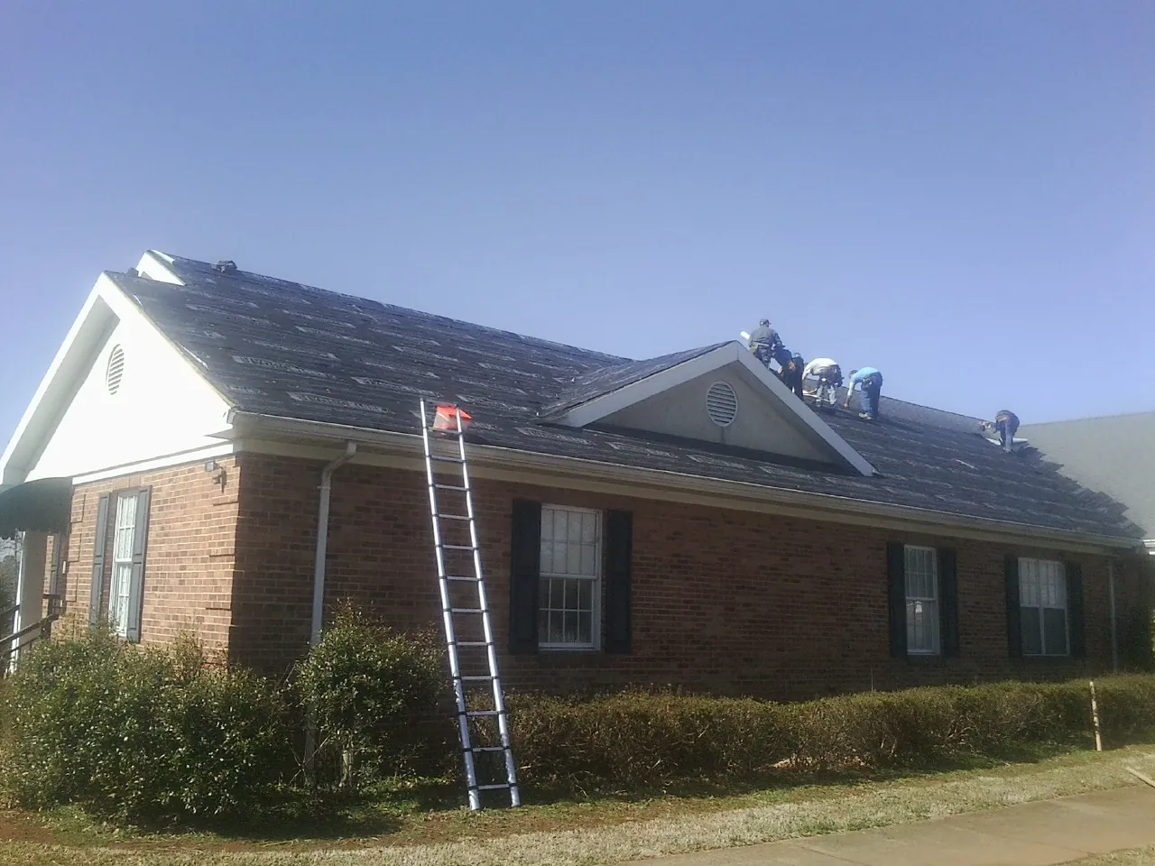 Crew tearing shingles off a brick ranch roof with a ladder set — Emergency Roof Repair work by our crew in East Stroudsburg