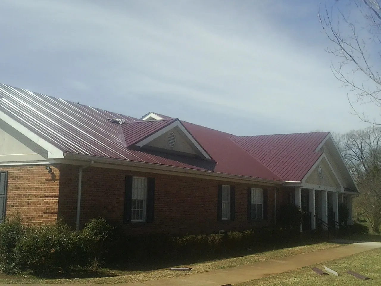 Red metal roof with gabled entries on a long brick building, from a Hail Damage Roof Repair job in East Stroudsburg