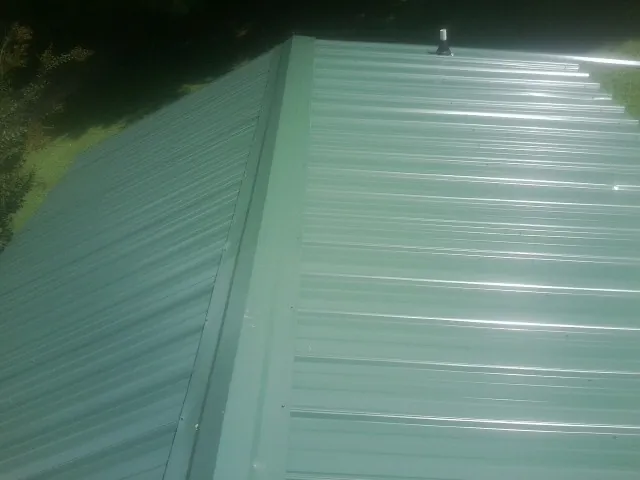 New green metal panels meeting at the ridge of a roof — Flat Roof Repair work by our crew in East Stroudsburg