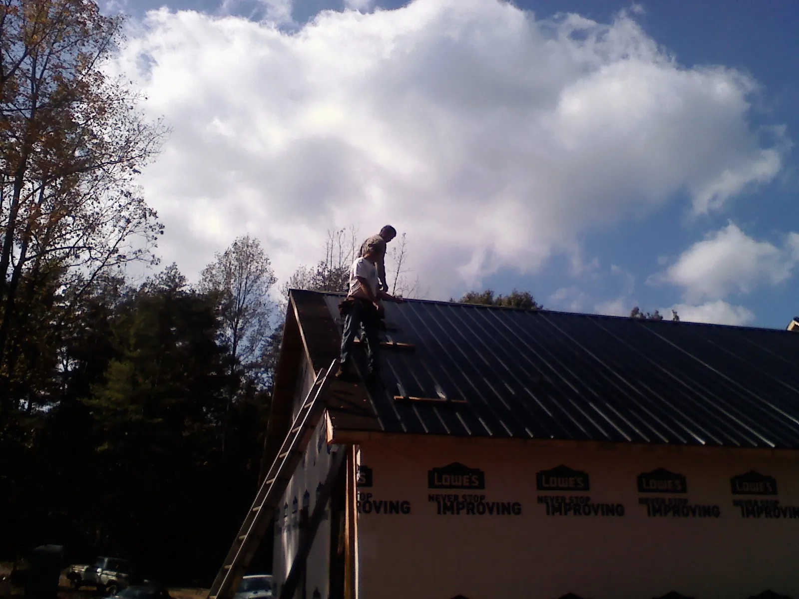 Roofer fastening dark metal panels high against a cloudy sky, from a Roof Inspection job in East Stroudsburg