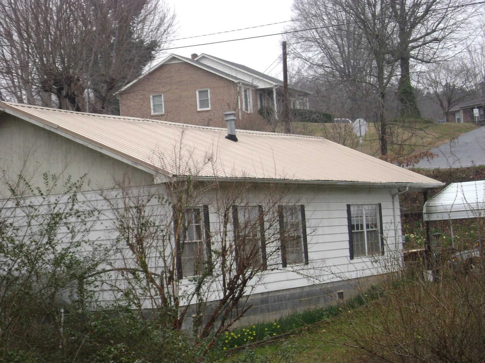 Tan metal roof on a white sided house set into a hillside — Commercial Roofing by Roofing Brothers in East Stroudsburg